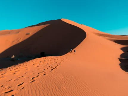 Traveler walking across the golden dunes of the Sahara Desert in Morocco