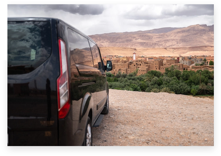 Ford Tourneo parked beside a palm-lined oasis near the Sahara Desert in Morocco.