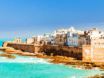 Essaouira coastline with historic city walls, whitewashed buildings, and turquoise Atlantic waters under a clear blue sky.