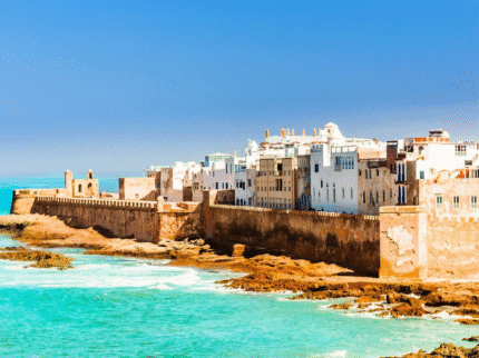 Essaouira coastline with historic city walls, whitewashed buildings, and turquoise Atlantic waters under a clear blue sky.
